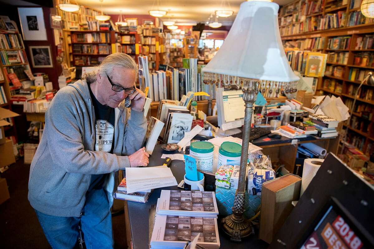 Eric Whittington takes a phone call from a customer for a book request at Bird & Beckett Books & Records, Tuesday, March 17, 2020, in San Francisco, Calif. Whittington is the owner of the store, located at 653 Chenery St. He lives in the same building as the bookstore, so is hunkering down in the shop to keep up with online sales and do curbside deliveries.