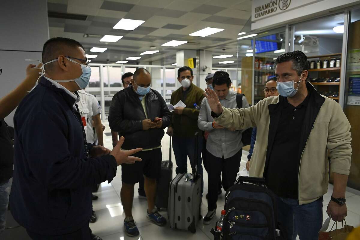 Passengers who were refused entry to El Salvador before they complete a quarantine, talk to an official (L) wearing a face mask as a precaution against the spread of the new coronavirus, COVID-19, at San Oscar Romero International Airport in San Luis Talpa, El Salvador, on March 12, 2020. - El Salvador banned entry to all foreigners for a period of 21 days in a bid to curb the spread of the coronavirus, the Central American country's president announced on March 11. Salvadorans arriving from countries where coronavirus has been declared would have to be quarantined for 30 days. (Photo by Marvin RECINOS / AFP) (Photo by MARVIN RECINOS/AFP via Getty Images)