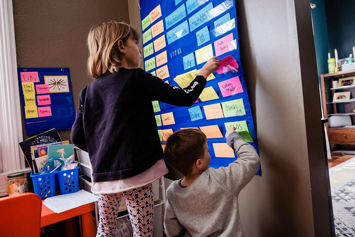 Lilly and Duke Butterfoss check on the cards in the “must do/may do” board that their mother Jennifer created for their homeschooling during the crisis in San Francisco, Calif. onTuesday, March 17, 2020.