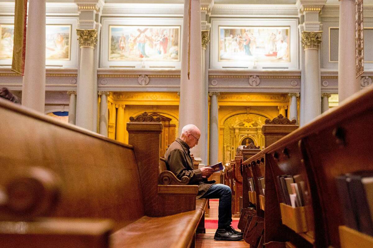 Tom Whelan of San Francisco sits by himself in a pew as he reads his personal bible while attending morning mass service at St. Ignatius Church in San Francisco, Calif. Friday, March 13, 2020. Friday's morning mass was moved from a smaller side parish to the main parish to help those worshipping keep their distance from one another amid the global thread of the Coronavirus.