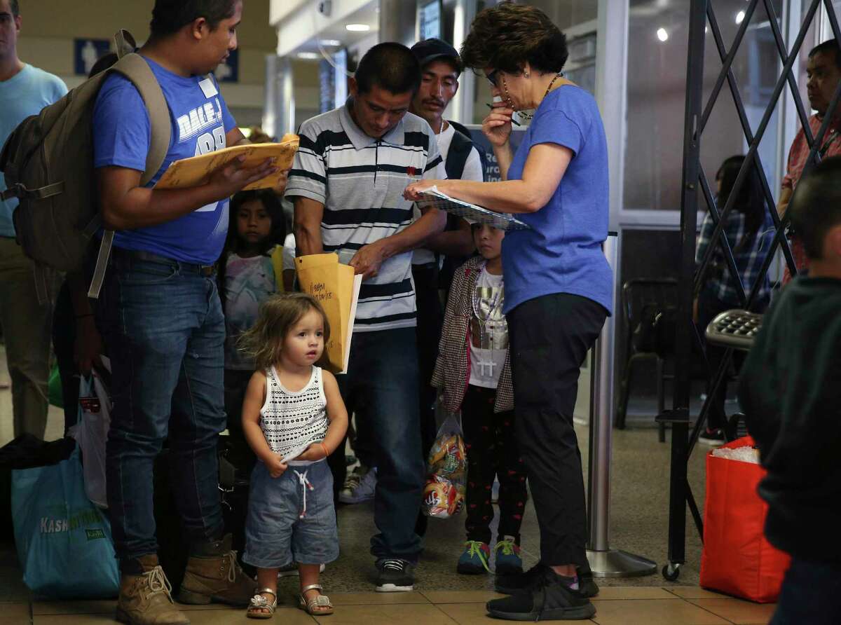 Juliet Giron, waits as her father, Brian Giron, 24, is helped by Interfaith Welcome Coalition volunteer Carolina Barrera at the Greyhound Bus station in San Antonio. They were kept together in family detention but later released as a family.