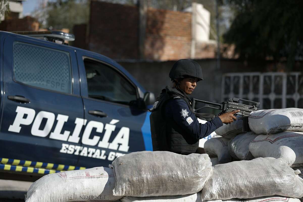 In this Feb. 12, 2020 photo, police stand guard behind a parapet of sandbags, at the entrance to Santa Rosa de Lima, birthplace of a local cartel that goes by the same name, in Guanajuato state, Mexico. Mexico's fastest-rising cartel, the Jalisco New Generation gang, has a reputation for ruthlessness and violence unlike any since the fall of the old Zetas cartel. In places like Guanajuato state it is fighting medieval-style battles for control of the state. (AP Photo/Rebecca Blackwell)