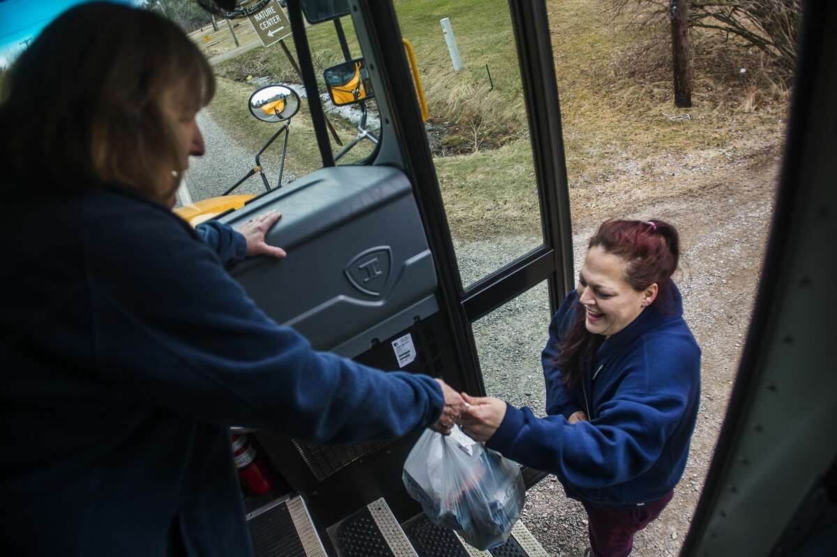 Glenna Hall, left, passes bags filled with bagged lunches and breakfasts to Emily Beach, right, as bus drivers and volunteers deliver meals for Bullock Creek students Wednesday, March 18, 2020. (Katy Kildee/kkildee@mdn.net)