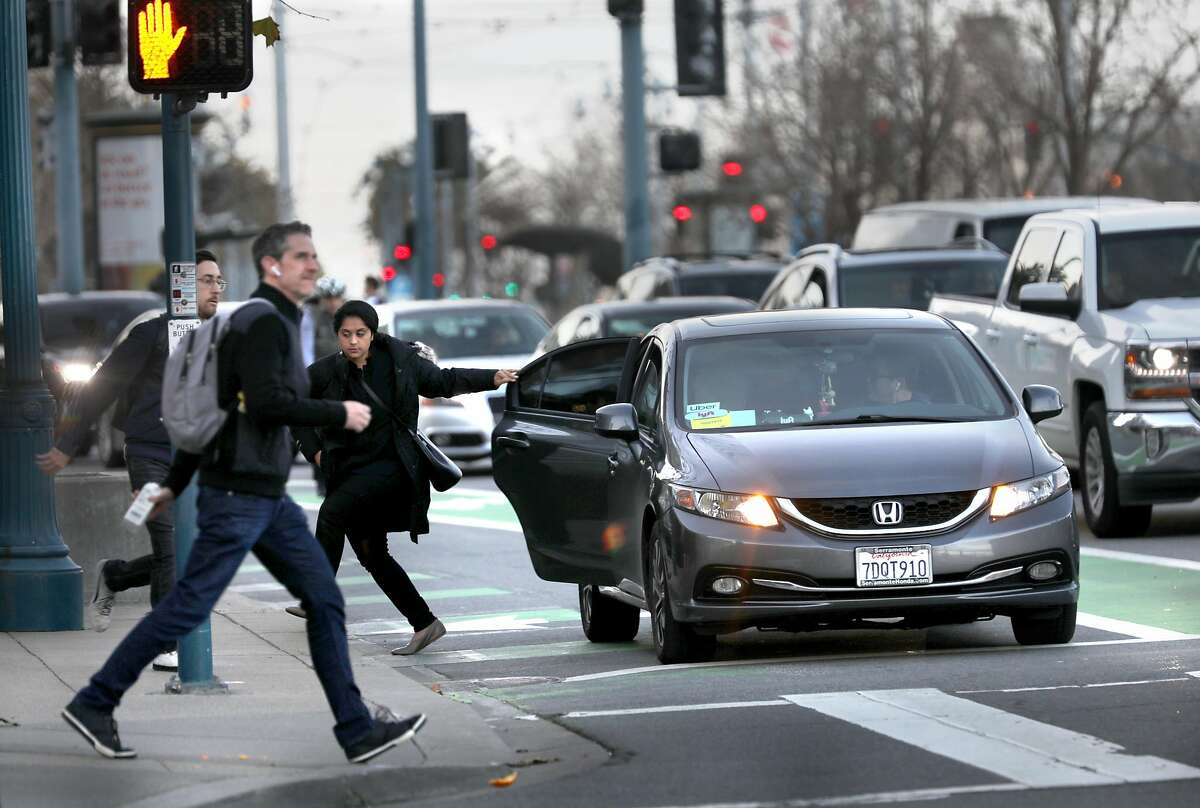 A passenger leaves a Lyft/Uber car on the Embarcadero at Mission St. as pedestrians cross the street on Wednesday, Jan. 29, 2020, in San Francisco, Calif.