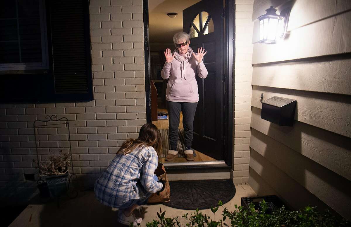 A woman who only gave her name as Mary (R) reacts as Alex Dewey (L) voluntarily delivers groceries and prescriptions to her doorstep in San Rafael on Monday, March 16, 2020.