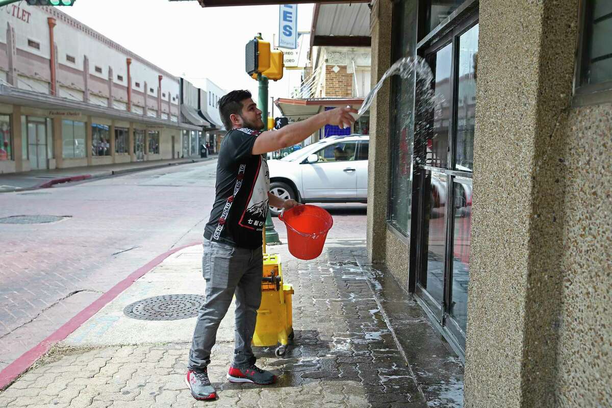 Luis Fernando Contreras, 23, washes windows at a downtown Laredo, Texas business, Wednesday, March 18, 2020. The City of Laredo issued an emergency order Wednesday in response to the coronavirus threat that will keep the public from gathering in groups of more than 10 and restaurants are only allowed to have takeout, delivery or drive-thru service for at least two weeks.