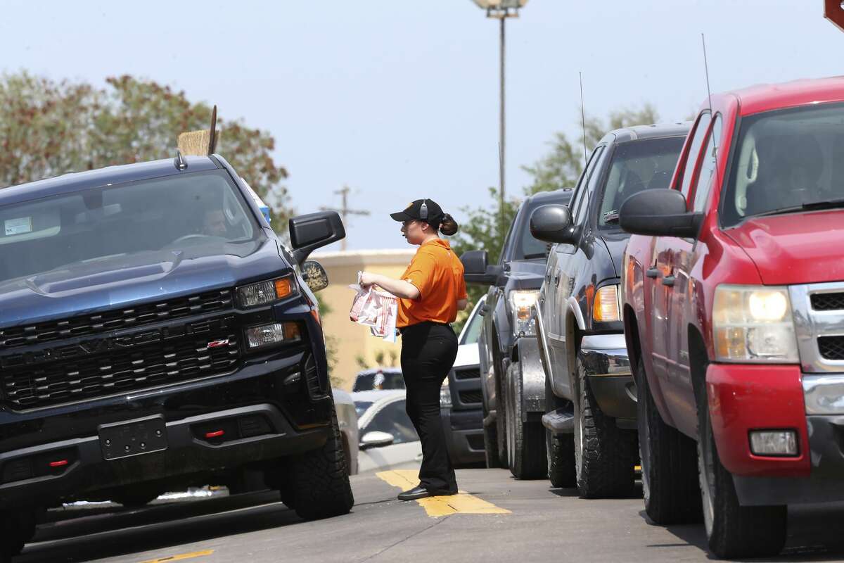 A Whataburger employee delivers meals to vehicles at a location in Laredo, Texas, Wednesday, March 18, 2020. Most major chain restaurants in Laredo closed their dining area and opened only with drive-thru, delivery or takeout service ahead of a lockdown order issued by the City of Laredo. The order takes effect at midnight Wednesday.