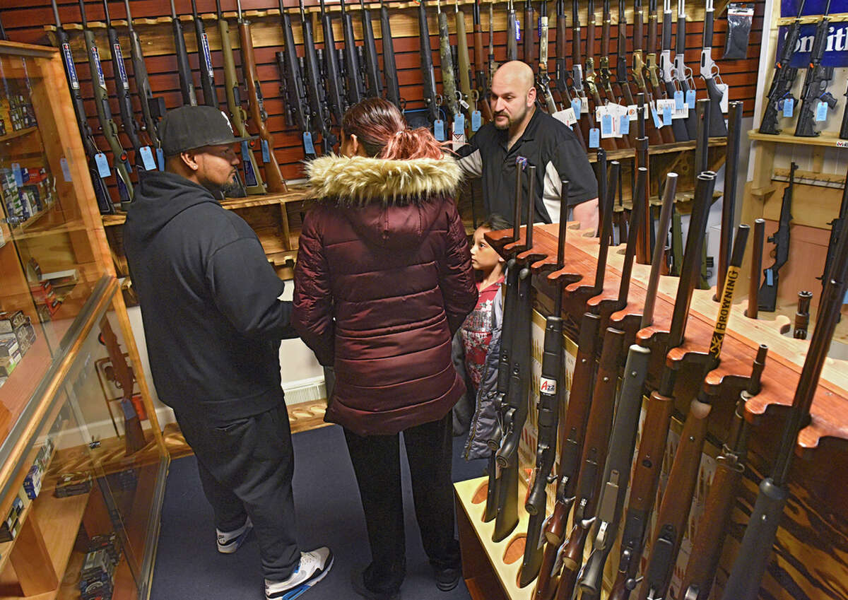 Craig Serafini, owner of Upstate Guns & Ammo, right, shows Kevin Atchana, left, who is shopping with his wife Ashley Harrichan and their daughter Alliyah Atchana, 6, some rifles at Serafini's gun store on Thursday, March 19, 2020 in Schenectady, N.Y. Alliyah was overheard asking her father "daddy, why do we have to buy a gun?" The parents were shopping for a gun to protect their family. (Lori Van Buren/Times Union)