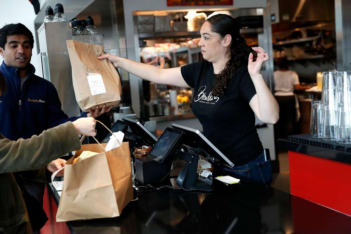 Tracey Anderson hands take out orders to customers while working at Brenda's in Oakland, Calif., on Wednesday, March 19, 2020.