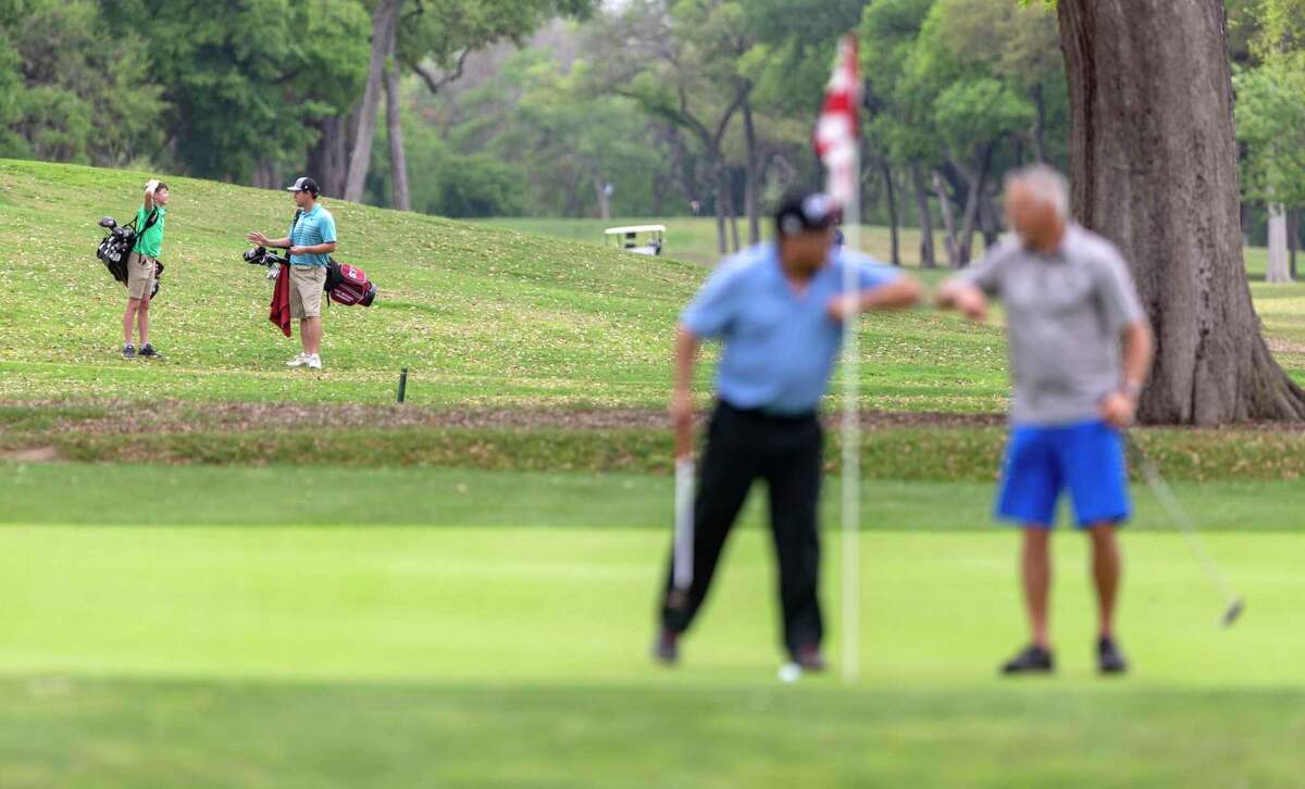 A pair of golfers, left, walk the Brackenridge Park golf course on March 18 as two others give an elbow high five to each other after making a putt. The governor ordered golf courses to close as non-essential businesses but state officials are interpreting the order as allowing walkers to play, with a minimum of course employees.