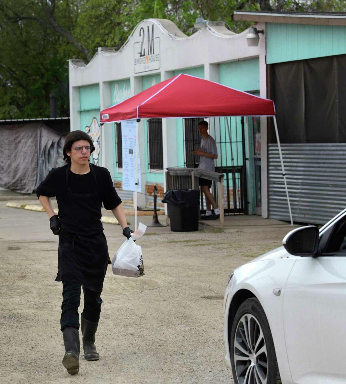 Nathaniel Campos rushes an order to a waiting customer at 2M Smokehouse. The acclaimed barbecue joint has now moved to a system where all of the food is sold to go with a makeshift drive-thru operation due to coronavirus precautionary measures.
