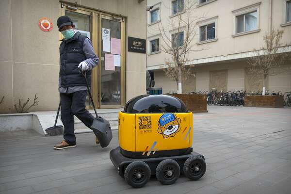 In this March 18, 2020, photo, a maintenance worker looks at a robot outside the offices of ZhenRobotics in Beijing. While other industries struggle, one robot maker says China's virus outbreak is boosting demand for his knee-high, bright yellow robots to deliver groceries and patrol malls for shoppers who fail to wear masks. (AP Photo/Mark Schiefelbein)