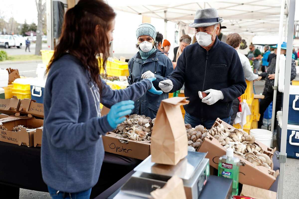 Lyla Moaven and Mansor Shokohi buy mushrooms from E&H Farms' Thea Tull at the Berkeley Farmers Market on Shattuck Avenue in Berkeley, Calif., on Wednesday, March 19, 2020.