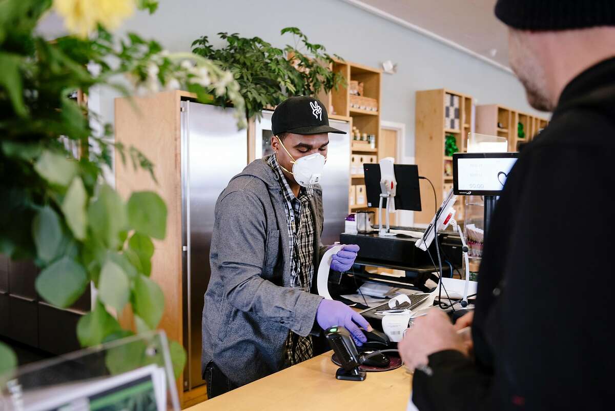 Sales associate Dustin Brown wears an N95 mask while ringing up customers at Harborside in Oakland, California, US, on Tuesday, March 17, 2020.