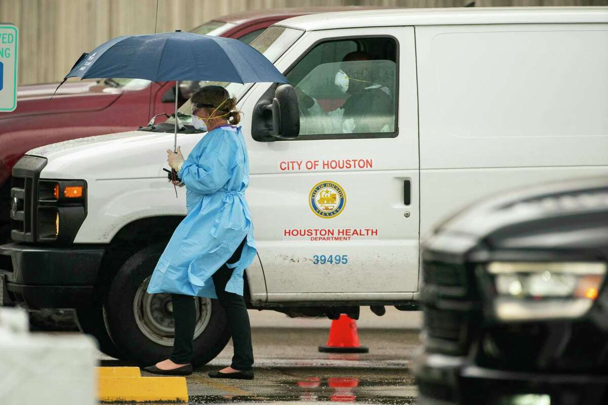 A healthcare professional walks through the line of cars waiting in line at the drive-thru testing center that opened to health care professionals and first responders, Friday, March 20, 2020, at Butler Stadium in southwest Houston. Everyone who arrived was already pre-screened and had to provide a unique ID number at the entrance to gain access. The city says the location will open to the broader public in the future.