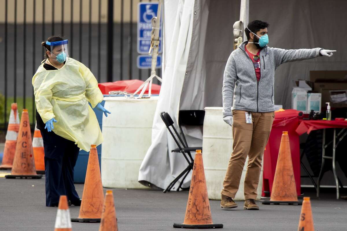 Health officials at a Verily coronavirus drive-thru test clinic wait for patients to instruct and verify before directing them inside the San Mateo County Event Center, Tuesday, March 17, 2020, in San Mateo, Calif.