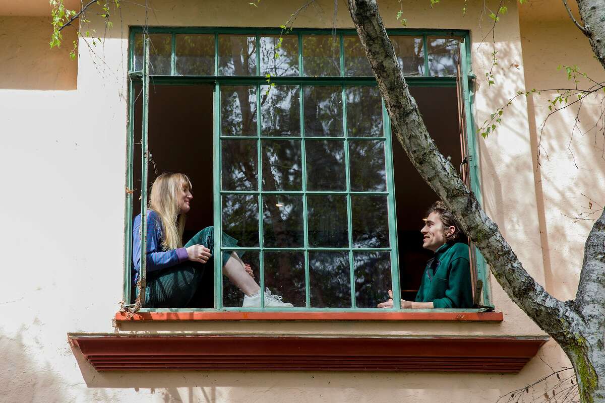 Samantha Dooley, 23, a copywriter for an ad agency and Liam Doran, 22, a UC Berkeley Grad Student studying Mechanical Engineering, pose for a portrait in the window of their home in Berkeley, Calif. Tuesday, March 17, 2020. Dooley is working from home as a result of the Coronavirus outbreak and Doran is working remotely to try and do as much as he can for his capstone project, although progress has been inhibited by the lack of access to campus machine shops and labs.