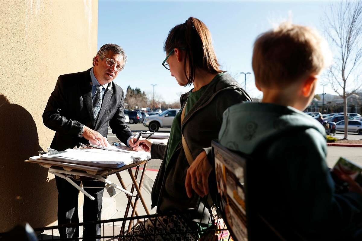 Kenn Zendels collects petition signatures from Kristi Hammer while her son, Lincoln, 2, waits outside of Safeway in Novato, Calif., on Wednesday, February 5, 2020.