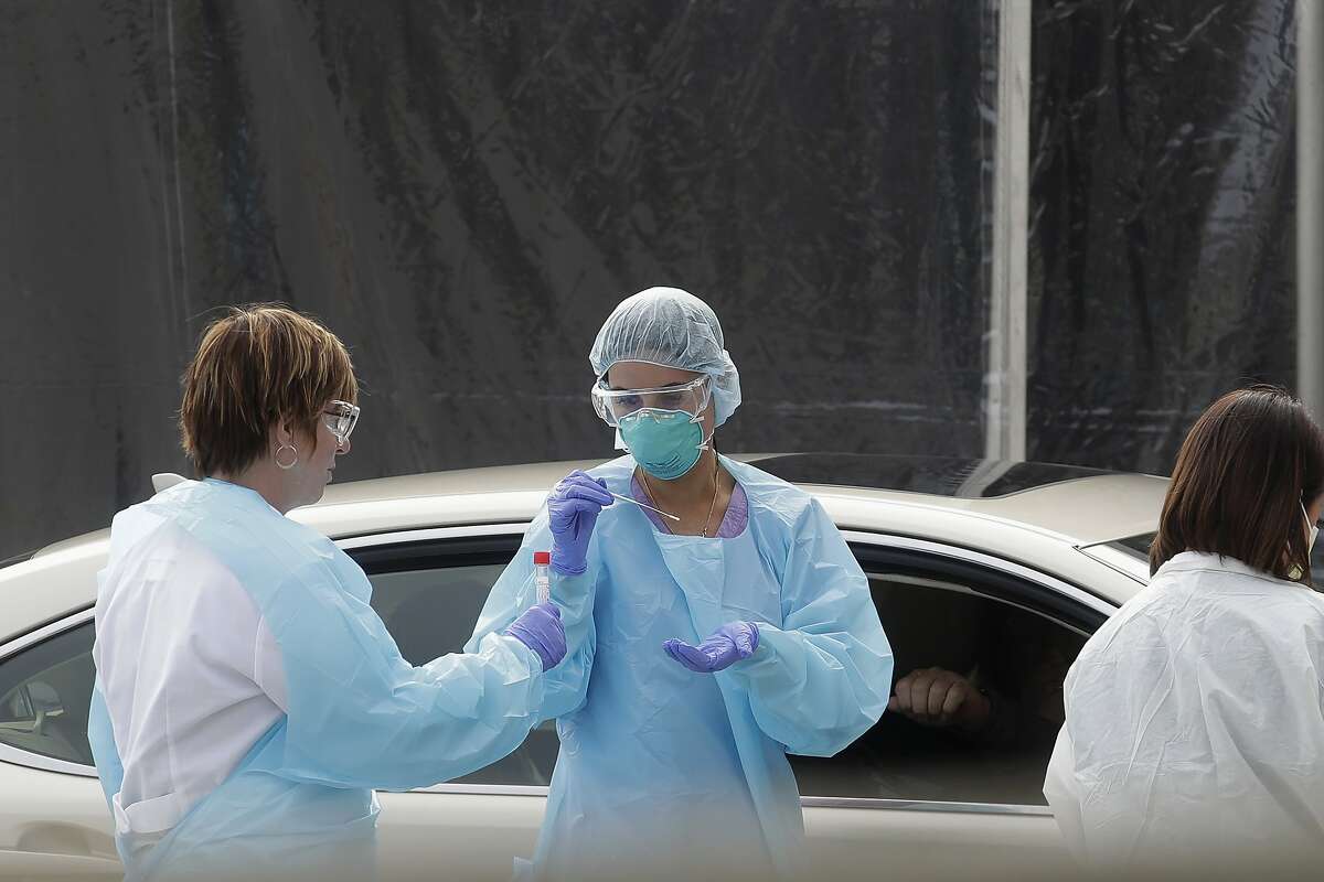FILE - In this March 12, 2020, file photo, health care personnel test a person in the passenger seat of a car for coronavirus at a Kaiser Permanente medical center parking lot in San Francisco. The Associated Press has found that the critical shortage of testing swabs, protective masks, surgical gowns and hand sanitizer can be tied to a sudden drop in imports of medical supplies. (AP Photo/Jeff Chiu, File)