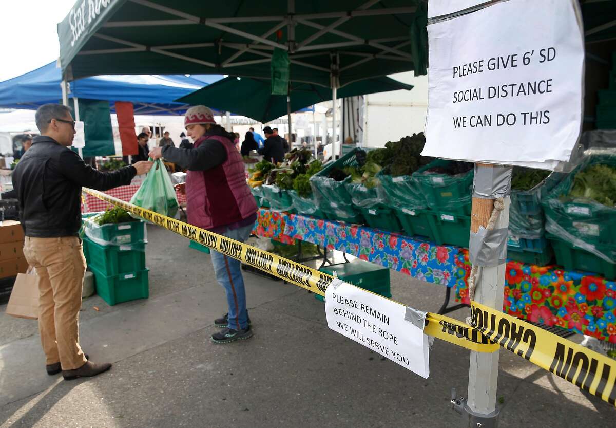 Patricia Buzzotta hands a bag of produce to a customer at the Star Route Farms stand in the Ferry Plaza Farmers Market in San Francisco, Calif. on Saturday, March 21, 2020 as the shelter in place order remains in effect to slow the spread of the coronavirus pandemic. Star Route Farms created a social distance zone in front of their stand.