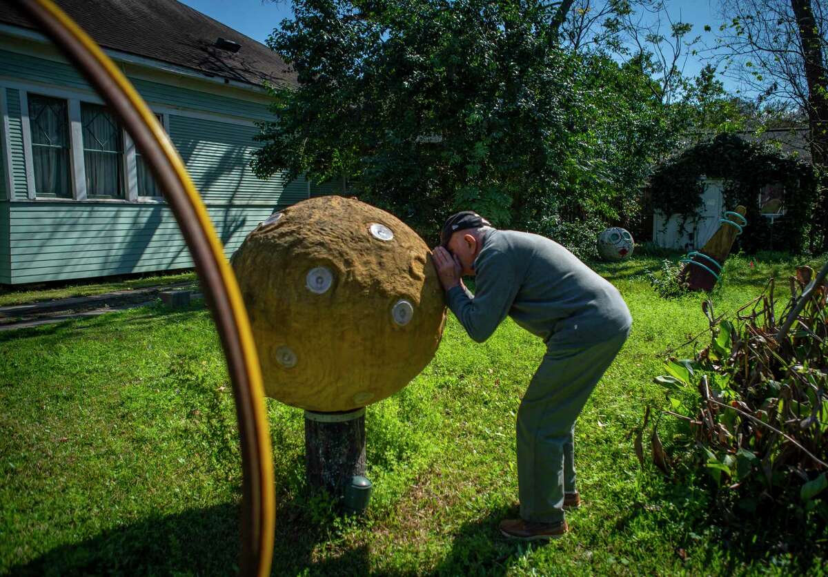 Arnold Van Ek peers into his sculpture "Dwarf Planet" to see the dinosaurs hidden inside where it stands in the empty lot across the street from his house that has served as an ad hoc neighborhood sculpture garden for almost 20 years, Friday, Feb. 21, 2020, in the Height's neighborhood of Houston.