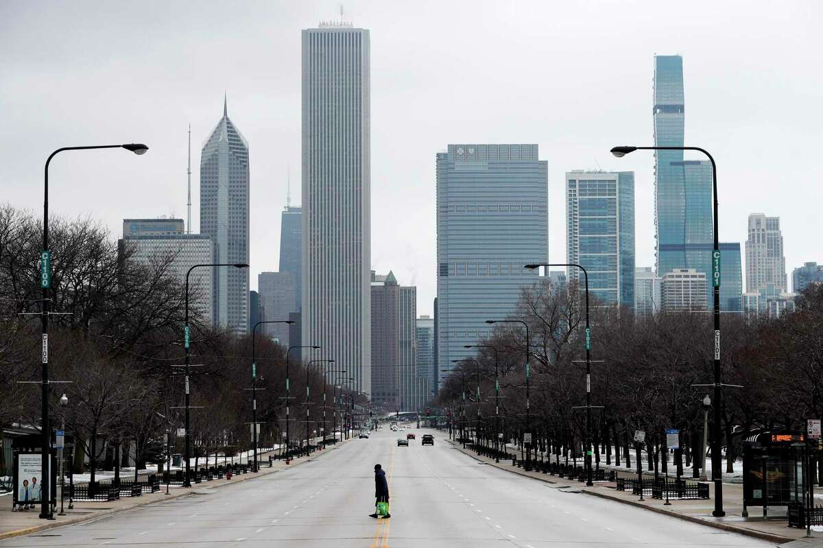 A woman walks across the usually busy Columbus Drive that splits Chicago's Grant Park in half, on the first work day since Illinois Gov. J.B. Pritzker gave a shelter in place order that began Monday, March 23, 2020.