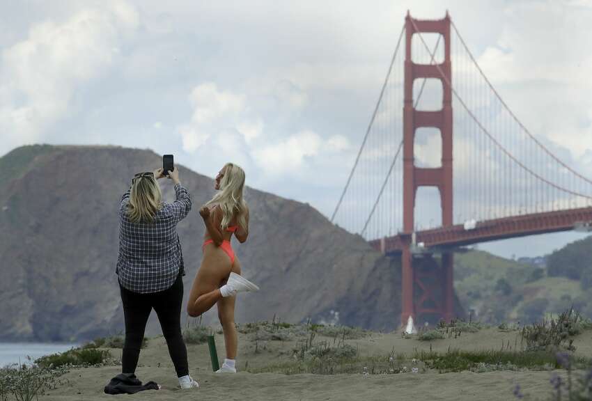 A bikini clad woman has her photo taken on Baker Beach near the Golden Gate Bridge on Sunday, March 22, 2020, in San Francisco. Some 40 million Californians are coping with their first weekend under a statewide order requiring them to stay at home to help curb the spread of the coronavirus.