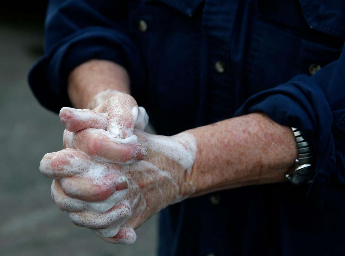 Annabelle Lenderink scrubs her hands while working at the Star Route Farms produce stand at the Ferry Plaza Farmers Market in San Francisco, Calif. on Saturday, March 21, 2020 as the shelter in place order remains in effect to slow the spread of the coronavirus pandemic.