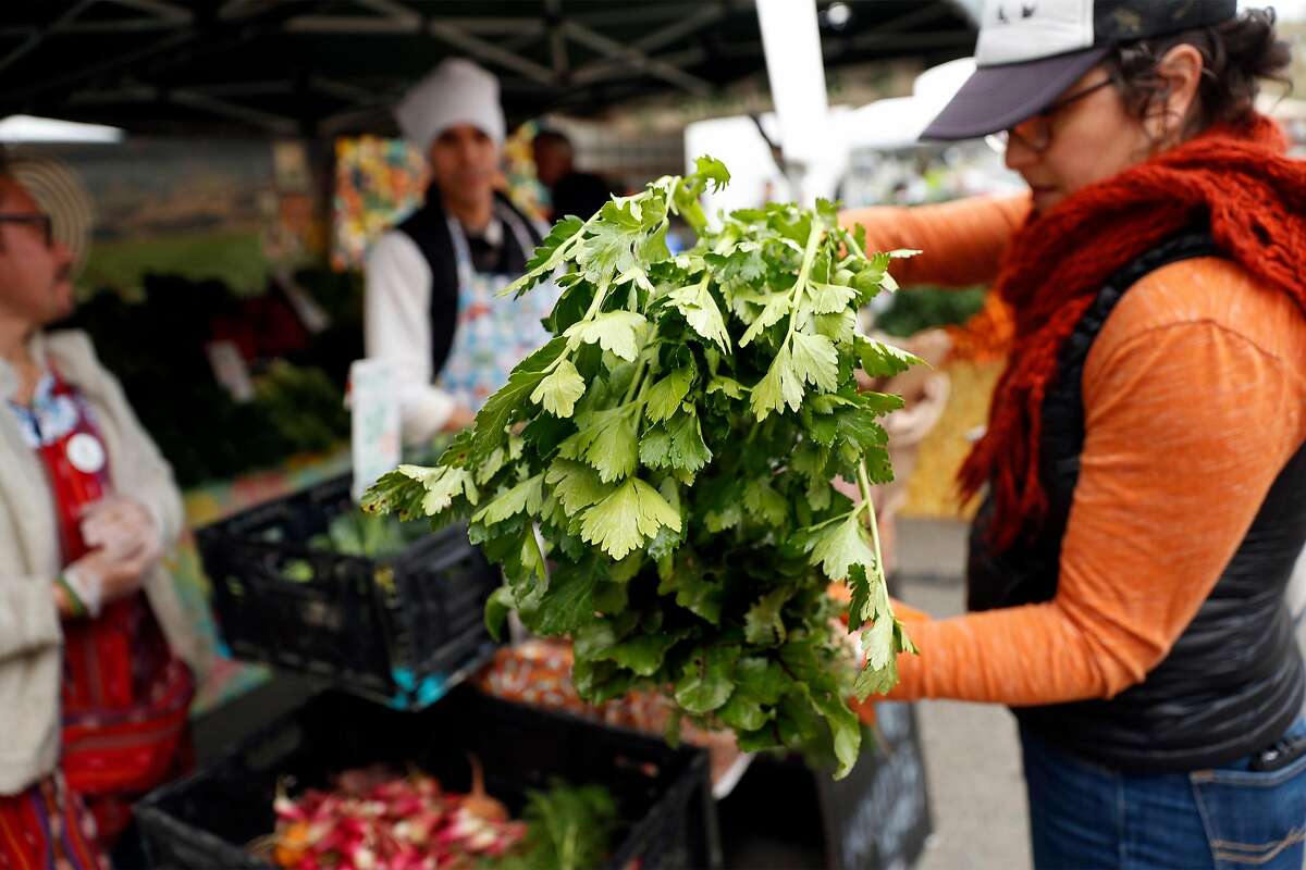 Vanya Goldberg of Oakland purchases vegetables from Gren Thumb Organics at the Berkeley Farmers Market on Shattuck Avenue in Berkeley, Calif., on Wednesday, March 19, 2020.