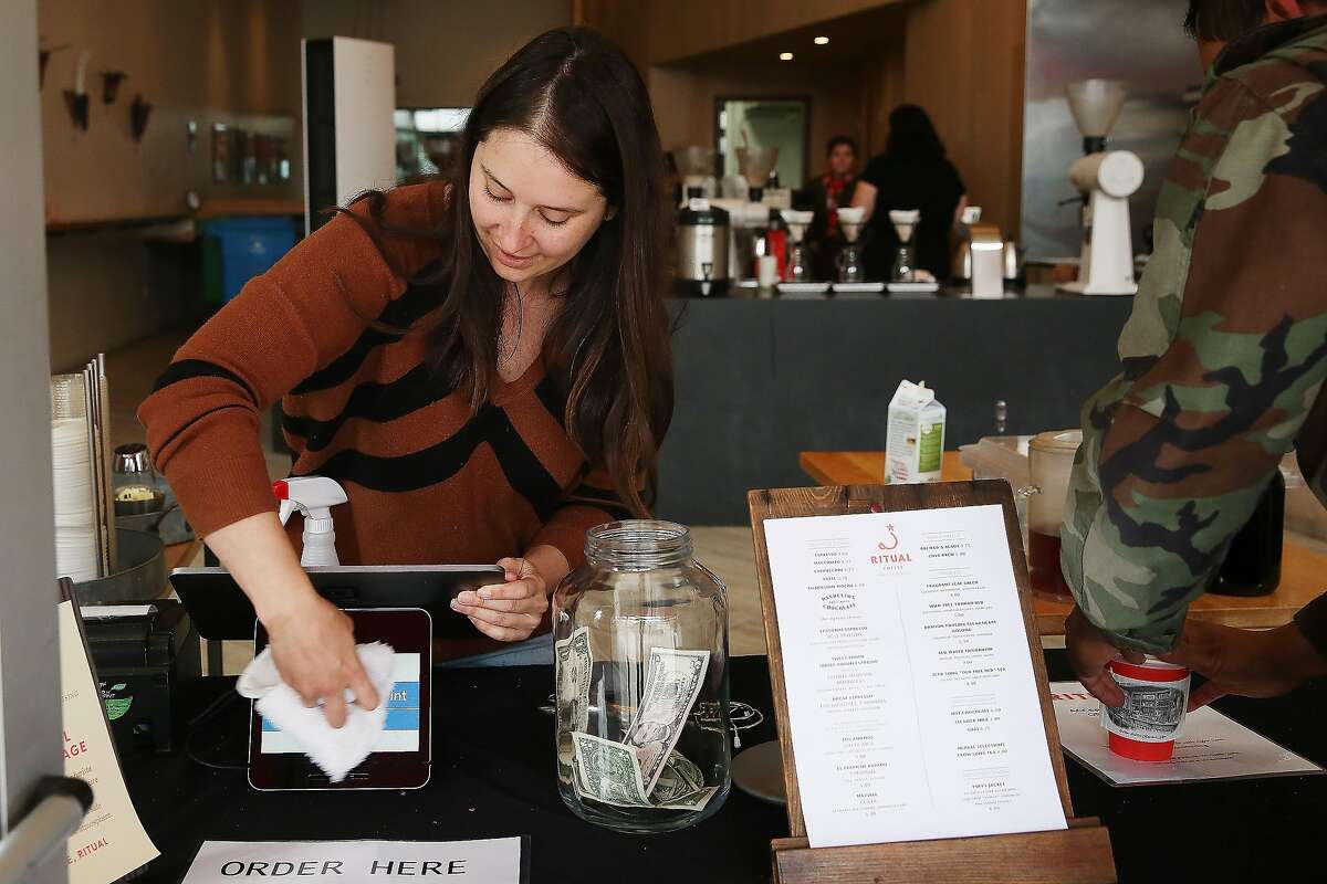 Emily Dobies, retail operations manger, wipes off a tablet screen inbetween customers using cashless payments at Ritual Coffee Roasters on Valencia Street on Tuesday, March 24, 2020 in San Francisco, Calif.