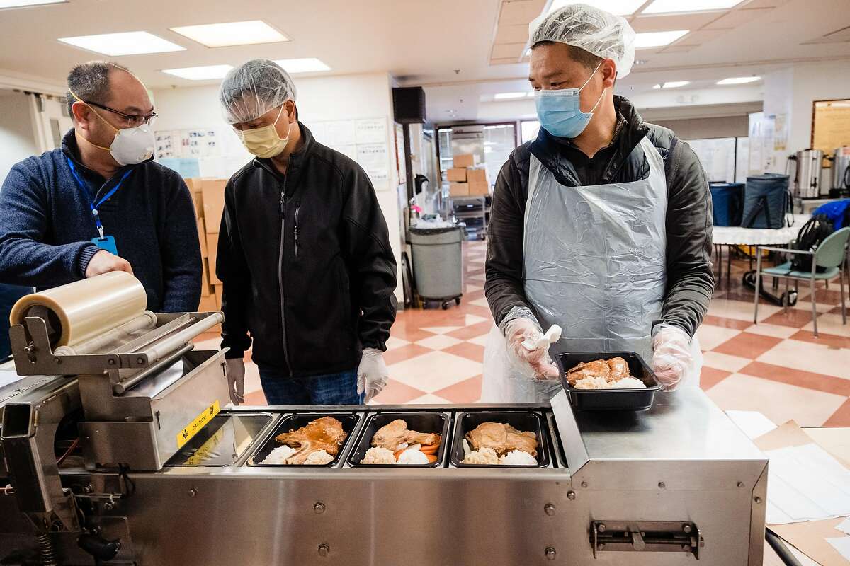 Stephen Ngan, left, Wei Ye, center and Chen Feng Bo run meals through a plastic wrapping machine meals before they get delivered to seniors at The Lady Shaw Senior Center in San Francisco, Calif. on Tuesday, March 24, 2020.