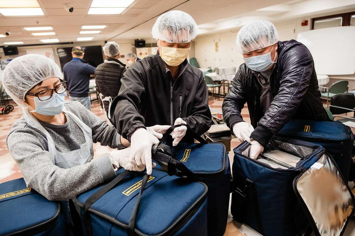 Hua Li, left, Wei Ye, center and Kyle Shiao box up meals to be delivered to seniors at The Lady Shaw Senior Center in San Francisco, Calif. on Tuesday, March 24, 2020.