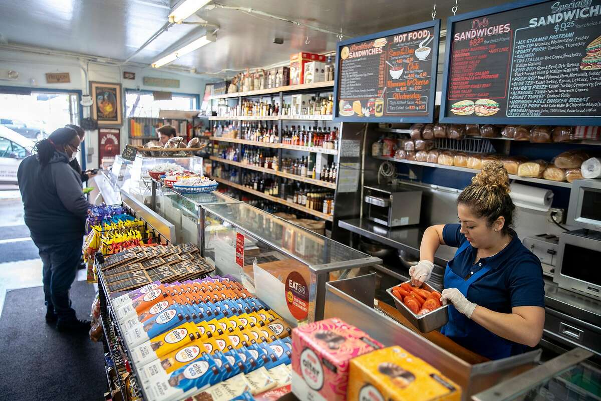 Sofia Saavedra stores food for closing hours as customers buy merchandise at Ted's Market & Deli on Tuesday, March 24, 2020, in San Francisco, Calif.