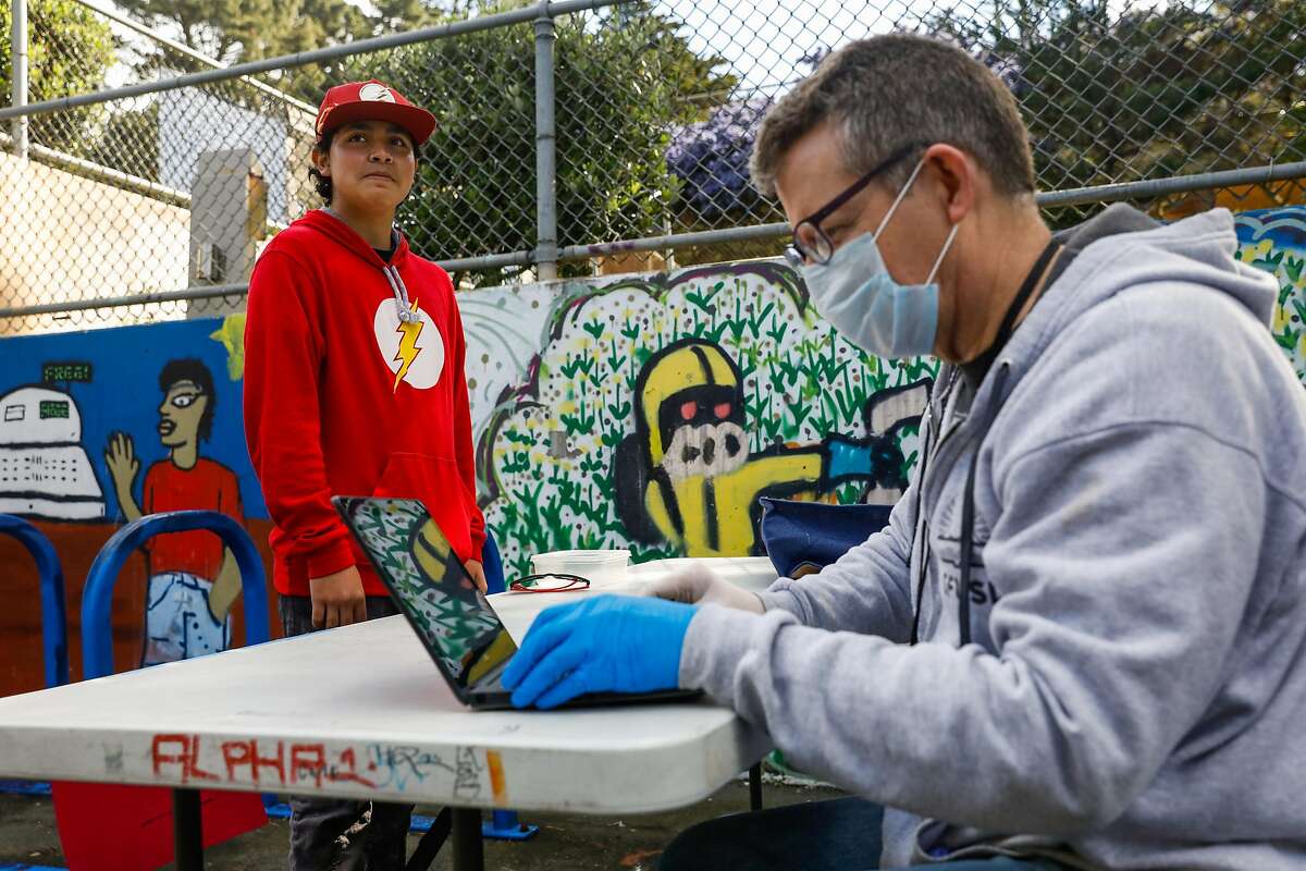 2020年3月25日星期三，加利福尼亚州旧金山，15岁的Brian Gonzalez(左)从SFUSD政策与规划主任Chris Armentrout手中拿起一本Chromebook。学校官员正在向学生分发chromebook，以便他们在冠状病毒关闭期间继续学习。