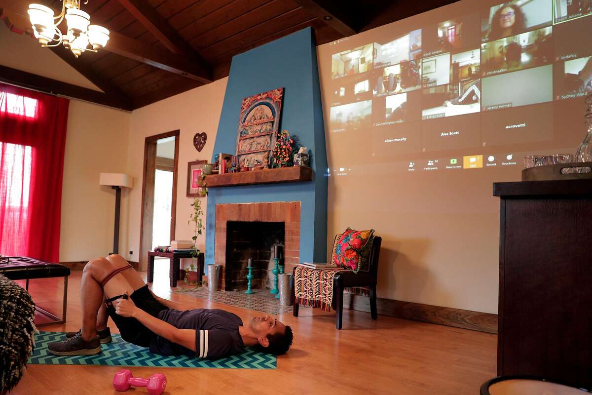 Daniel Vasquez works out in his living room during a streamed class by Sweat in Place using Zoom to share workouts remotely in Oakland, Calif., on Tuesday, March 24, 2020.