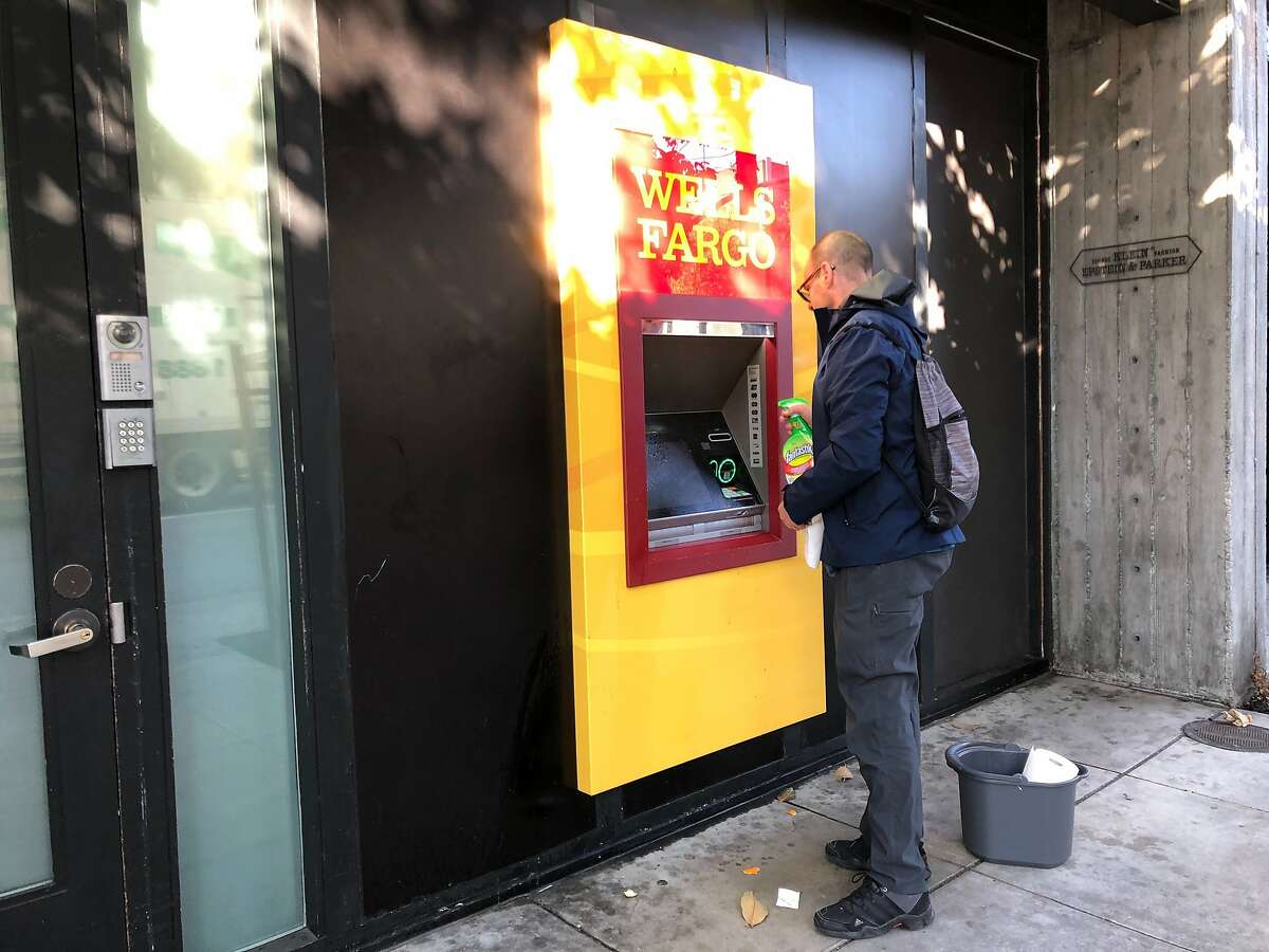 David Mayer, a personal trainer and yoga instructor in San Francisco, sprays down a Wells Fargo ATM machine before using it in San Francisco on Friday, March 20, 2020. Nearly 40 million people in California awoke Friday to the reality of a near lockdown to prevent the spread of coronavirus. (AP Photo/Olga R. Rodriguez)