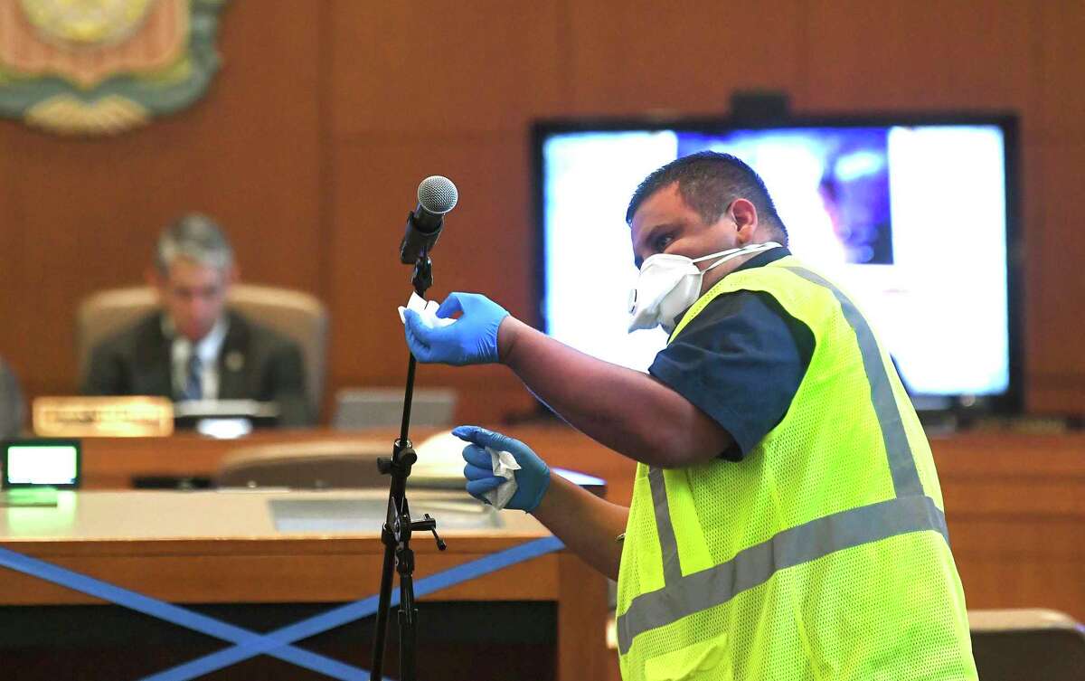 David Torres wipes down the microphone between speakers during a San Antonio City Council meeting in March. Some council members attend meetings in person; others attend via videoconferencing. Residents may sign up to comment in person or send in their comments by email or voice mail, among other methods of communication.