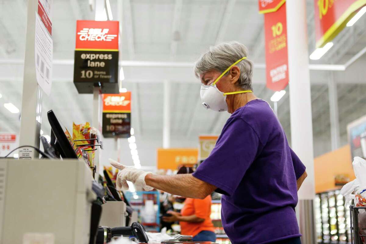 Connie Herring wears a gloves and mask as she uses the self check out line, Wednesday, March 25, 2020, at H-E-B in Bellaire. Herring said she started wearing a mask in public about a week ago. Her husband had a a major surgery two weeks ago, and she does not want to bring anything home with her, she said.