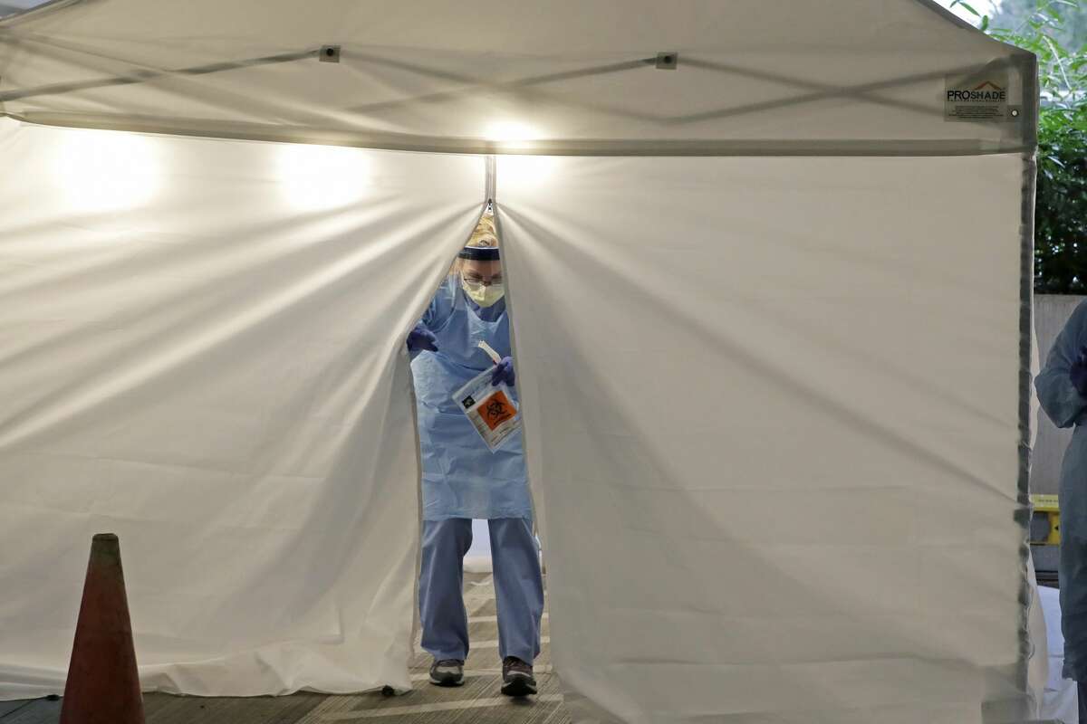 A nurse at a drive up COVID-19 coronavirus testing station set up by the University of Washington Medical Center exits a tent while holding a bag containing a swab used to take a sample from the nose of a person in their car, Friday, March 13, 2020, in Seattle. UW Medicine is conducting drive-thru testing in a hospital parking garage and has screened hundreds of staff members, faculty and trainees for the COVID-19 coronavirus. U.S. hospitals are setting up triage tents, calling doctors out of retirement, guarding their supplies of face masks and making plans to cancel elective surgery as they brace for an expected onslaught of coronavirus patients. (AP Photo/Ted S. Warren)