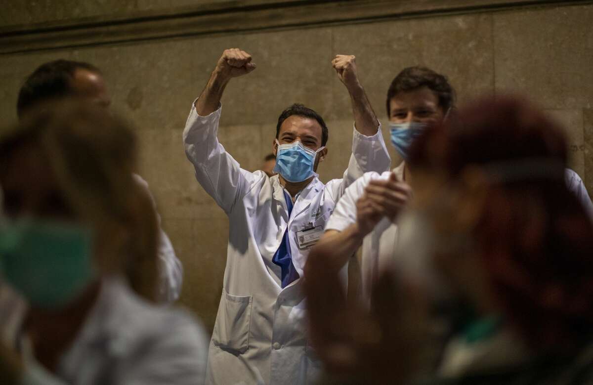 Health workers react as people applaud from their houses in support of the medical staff that are working on the COVID-19 virus outbreak at the main gate of the Hospital Clinic in Barcelona, Spain, Thursday, March 26, 2020.