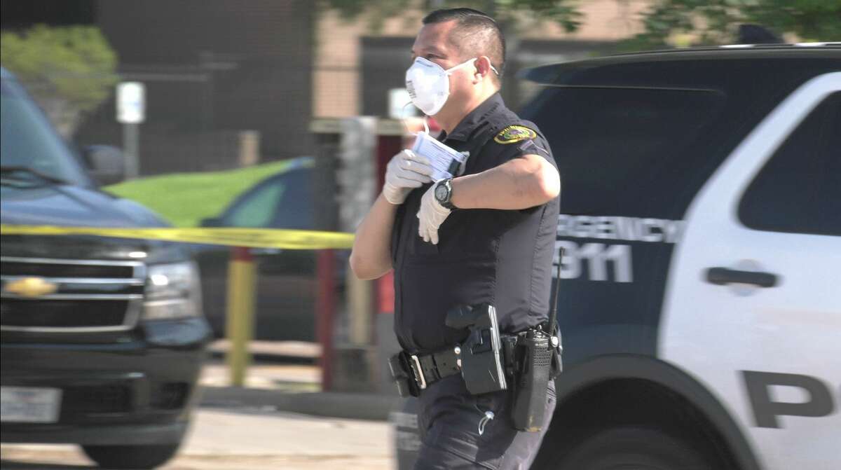 A mask-wearing Houston police officer investigates a deadly shooting in the 9800 block of Beechnut on Friday, March 27, 2020.
