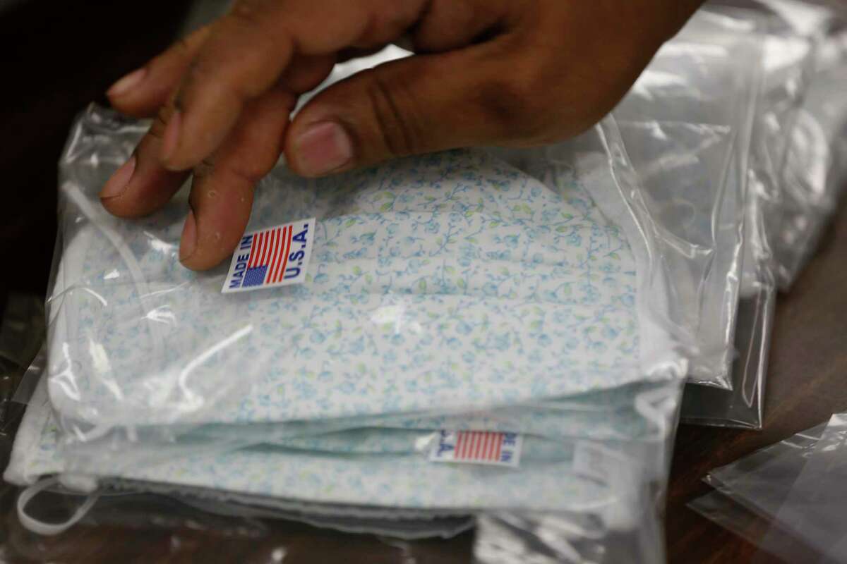 David Cardona places a made in USA sticker to a packaged face mask at Paty, Inc. Thursday, March 26, 2020, in Houston. Paty, Inc. has been manufacturing clothing for 65 years, but as the novel coronavirus has spurred demand for medical supplies, it has retooled its operations to produce face masks and surgical gowns.