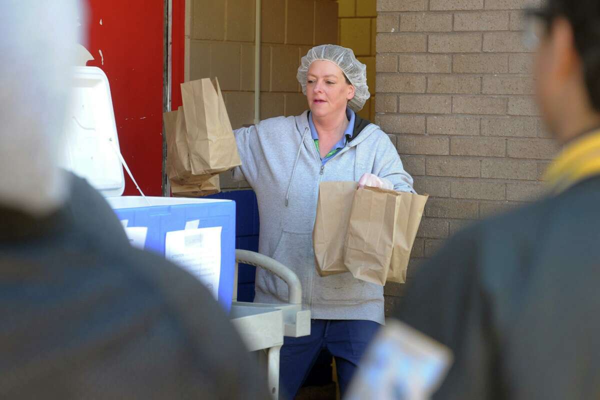 Cafeteria manager Janice Northrop carries bags of grab-and-go meals for students at Curiale School, in Bridgeport, Conn. Nov. 27, 2020. Bridgeport schools have expanded the program from breakfast and lunch to also include items for dinner meals.