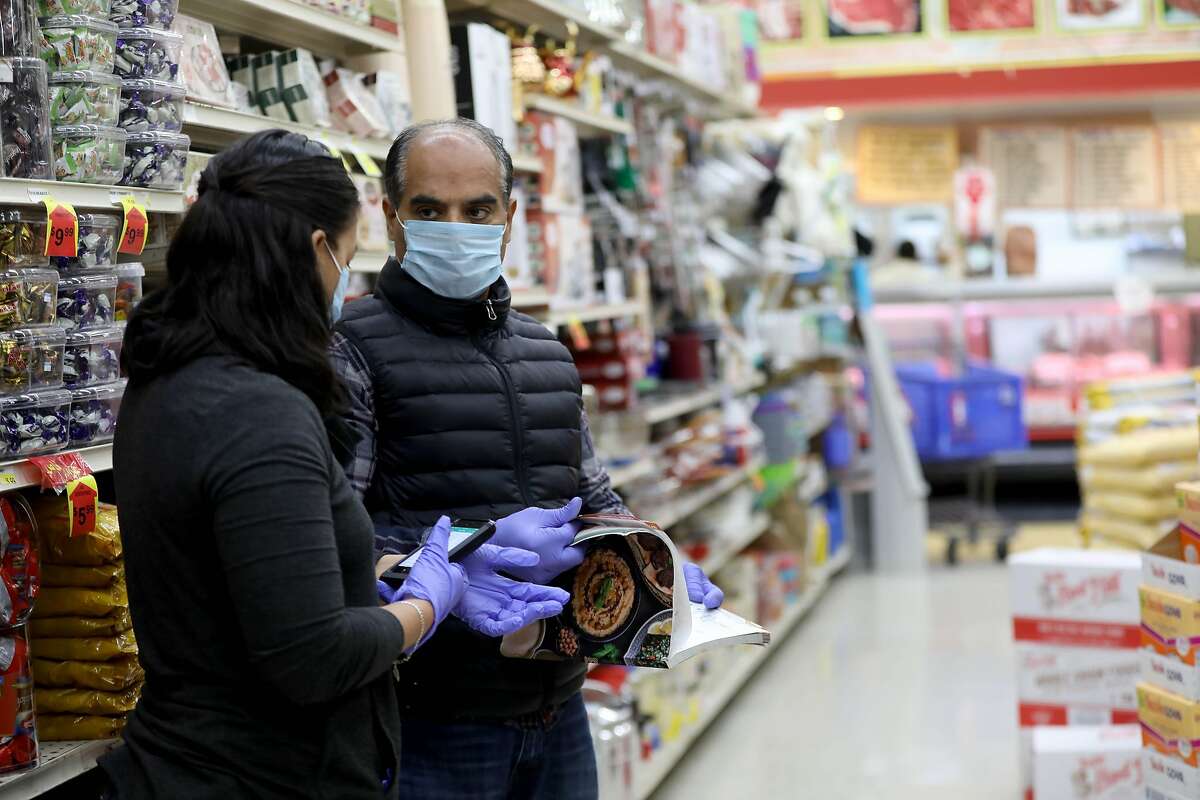 Alejandra Cabrales, left, a salesperson, works with Ali Albasiery, the operator at Shop Rite, located at 5800 Bancroft Ave., on Thursday, March 26, 2020, in Oakland, Calif.
