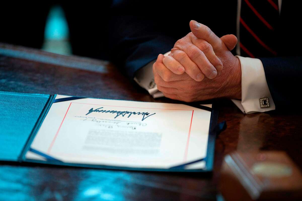 US President Donald Trump signs the CARES act, a $2 trillion rescue package to provide economic relief amid the coronavirus outbreak, at the Oval Office of the White House on March 27, 2020. - After clearing the Senate earlier this week, and as the United States became the new global epicenter of the pandemic with 92,000 confirmed cases of infection, Republicans and Democrats united to greenlight the nation's largest-ever economic relief plan. (Photo by JIM WATSON / AFP) (Photo by JIM WATSON/AFP via Getty Images)
