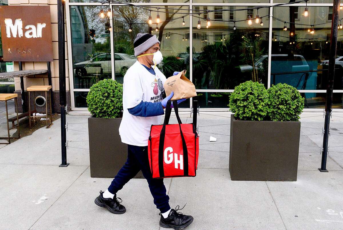 Grubhub driver David Augusta carries an order from alaMar on Friday, March 27, 2020, in Oakland, Calif. The restaurant has seen business increase as customers seek take-out and delivery options under coronavirus stay-at-home orders.