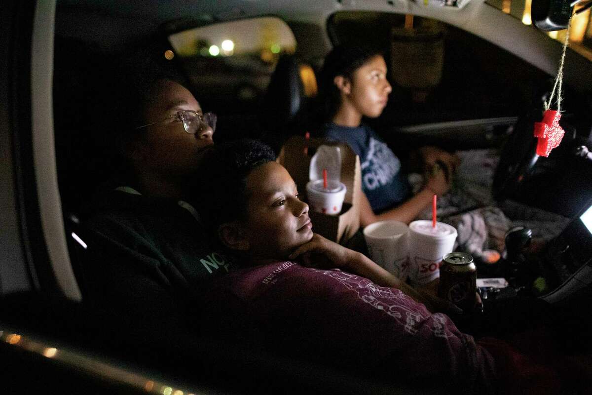 Lazarus Brown rests with his sister, Alana, left, and Malia Bennett, right, as they watch a projected movie at the EVO Entertainment facility in Schertz on Friday night, March 27, 2020. The EVO Drive-In showed "Spider-Man Homecoming," free of charge, although patrons were encouraged to buy food and beverage to support employees working the show. The event provided a chance for people to see a movie while maintaining social distancing to combat the spread of the coronavirus.