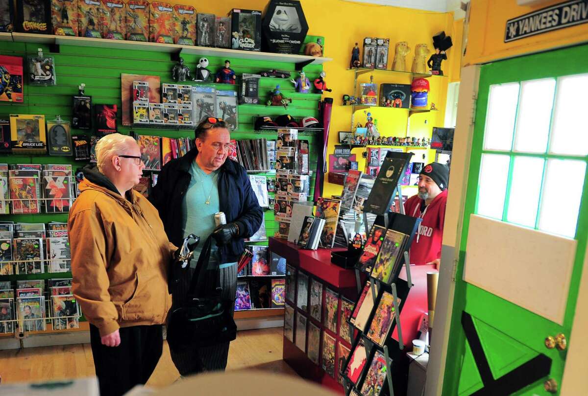 Rogue Comics owner Michael Fuller, at right, waits on brothers Richard and Kevin Kane, center, at the store in the Black Rock section of Bridgeport, Conn., on Wednesday Mar. 25, 2020. Owner Michael Fuller is trying to get a waiver from the state to remain open. For now he is letting customers come by appointment only.