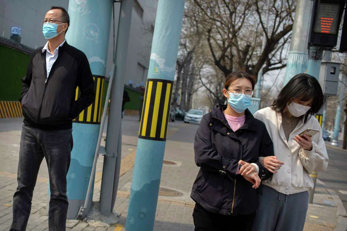 People wearing face masks wait to cross a street in Beijing on March 31, 2020. The U.S. Centers for Disease Control and Prevention reportedly is considering its guidance on face mask use. Its current recommendation is that people who are well should not wear them in public.