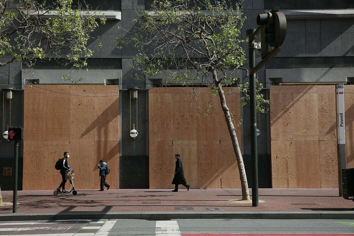 Pedestrians walk past a part of Westfield Mall that has been boarded up on Friday, March 27, 2020 in San Francisco, Calif.